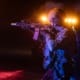 Tactical soldier aiming rifle with red and blue lights in the background at night.
