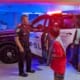 Police officer showing a police car to a group of children in a parking garage, with bright lights illuminating the scene.