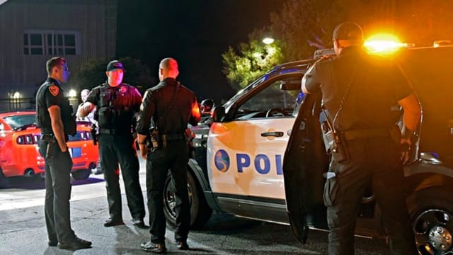 Police officers standing near patrol cars with flashing lights during a nighttime operation.