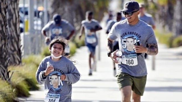 Father and daughter running together in a charity 5k event wearing matching gray shirts with a man's face printed on them.