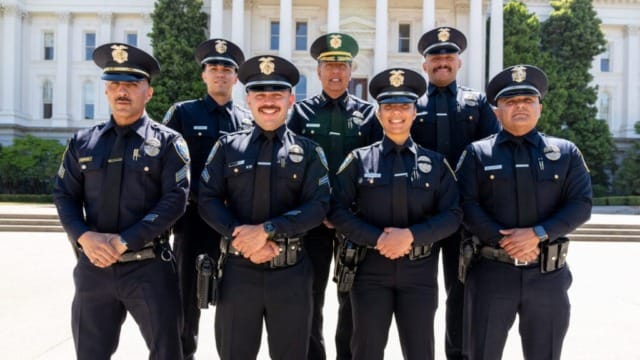 Group of uniformed police officers standing in front of a government building with trees in the background