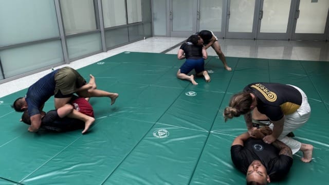 People practicing grappling techniques on mats in a spacious indoor training area.