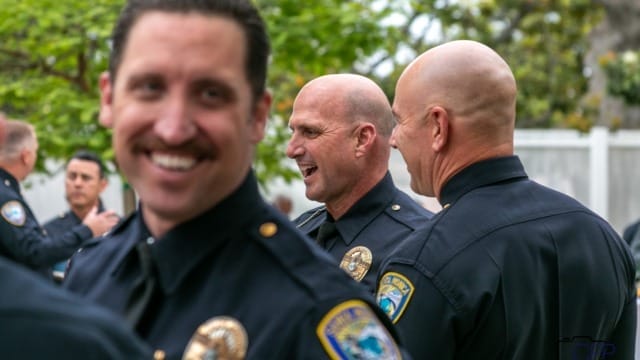 Police officers in uniform smiling and talking outdoors at a community event.