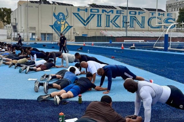People doing push-ups on a blue athletic track with a large Viking-themed mural in the background.