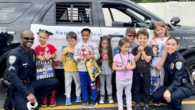 Police officers posing with a group of smiling children in front of a police car in a community event.