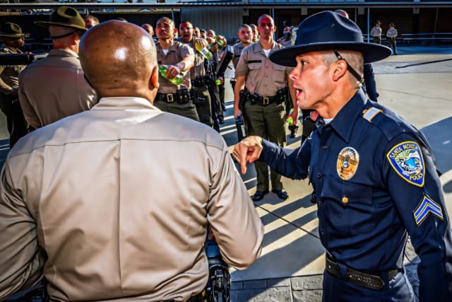 Police officer instructing recruits standing in formation outdoors, highlighting training and discipline in law enforcement.