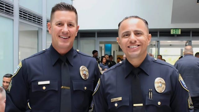Two police officers in uniform smiling indoors at an event.
