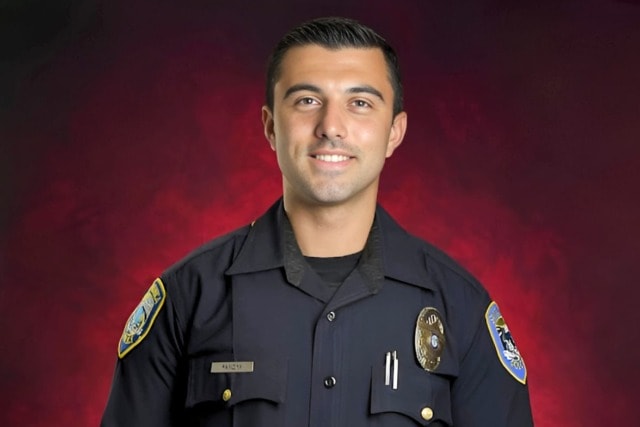 Police officer in uniform smiling against a red background.