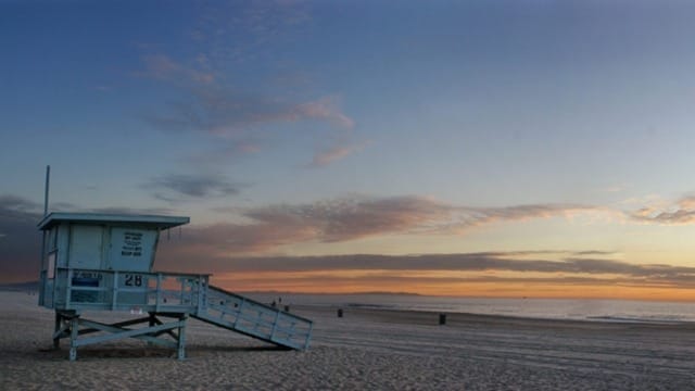 Lifeguard tower on an empty beach at sunset with a vivid sky in the background.