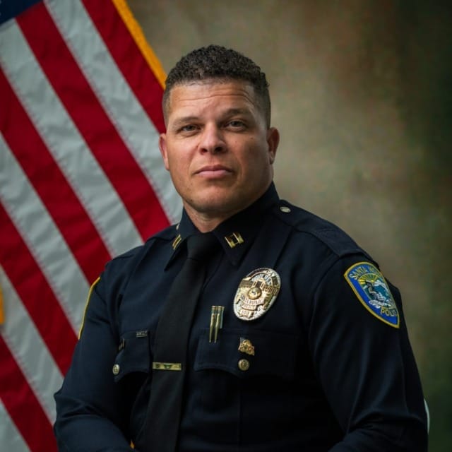 Police officer in uniform seated in front of an American flag backdrop